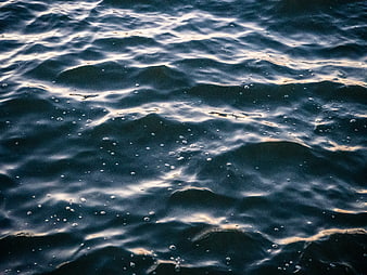 Close-up of dark ocean waves with bubbles and golden light