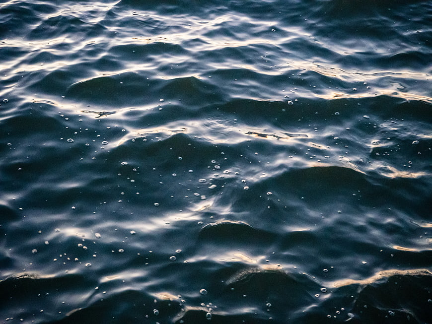 Close-up of dark ocean waves with bubbles and golden light