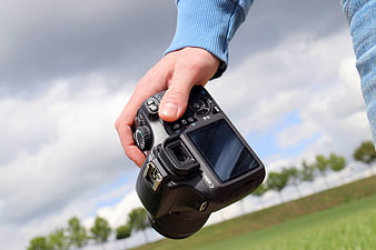 Hand holding DSLR camera against cloudy sky background