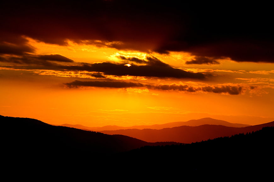 Dramatic Orange Sunset Over Silhouetted Mountain Range Landscape
