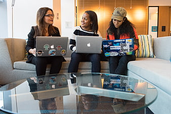 Three female developers collaborating on laptops in modern office lounge