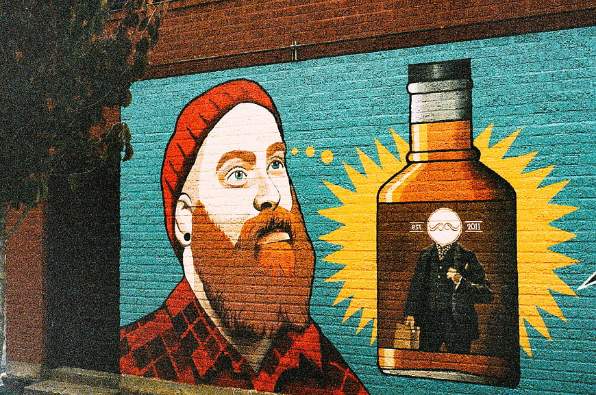 Colorful street art mural of bearded man and whiskey bottle