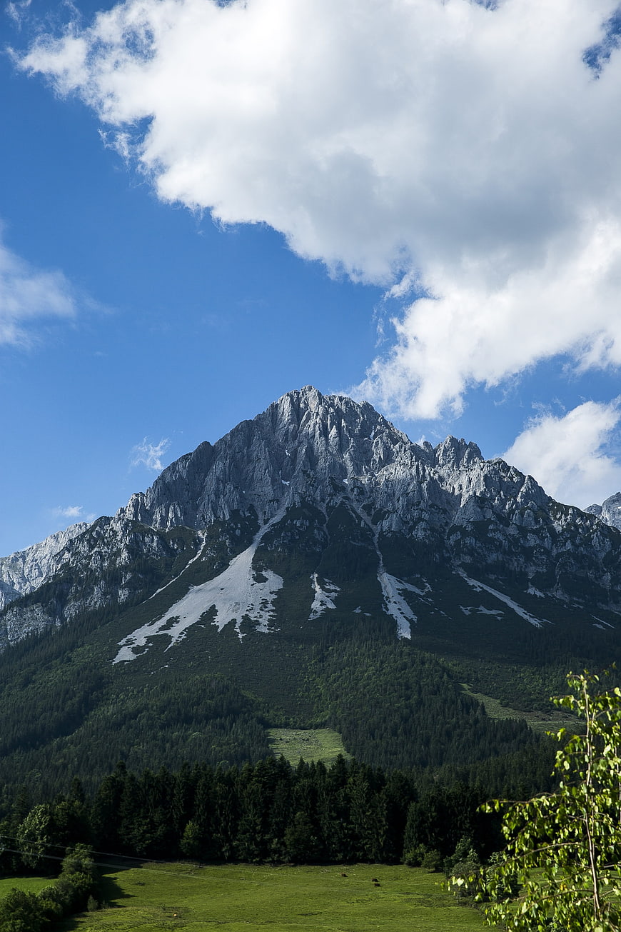 Majestic Alpine Mountain Peak with Snow Patches and Forest