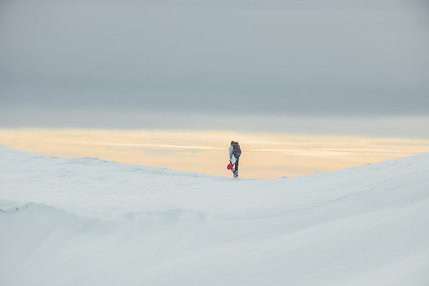 Lone hiker walking on snowy ridge at sunset