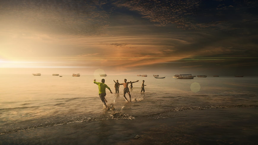 Boys Running in Ocean at Sunset with Boats