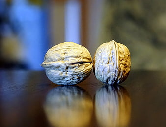 Two whole walnuts on a dark wooden table with reflection