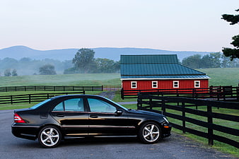 Black luxury sedan parked near red barn in countryside