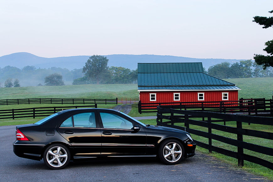 Black luxury sedan parked near red barn in countryside