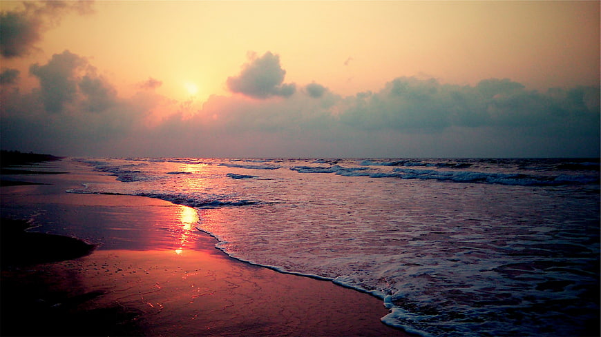 Sunrise over ocean waves on sandy beach