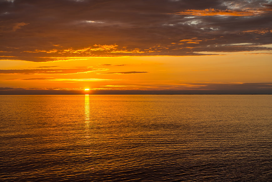 Golden Sunset Over Calm Ocean With Dramatic Clouds And Sun Reflection