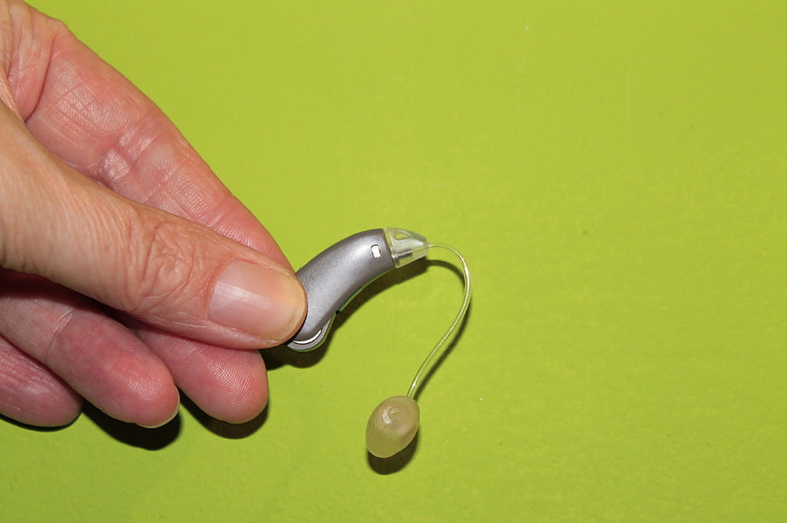 Hand holding a silver hearing aid against a bright green background