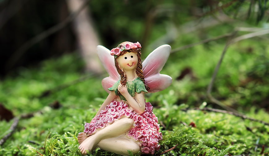 Cute ceramic fairy figurine sitting on green moss in a forest