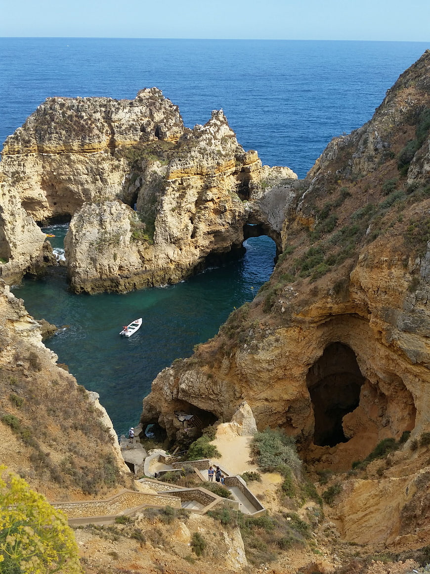 Dramatic coastal cliffs with sea arch and boat in cove