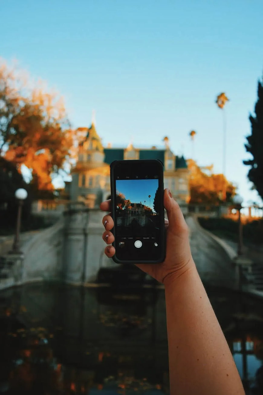 Hand holding smartphone photographing grand mansion at sunset