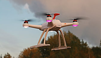 White quadcopter drone flying outdoors with glowing pink lights