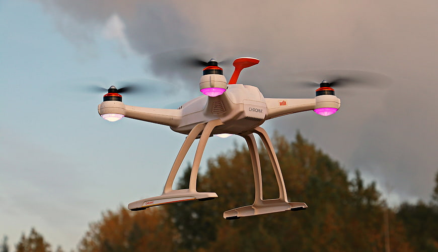 White quadcopter drone flying outdoors with glowing pink lights