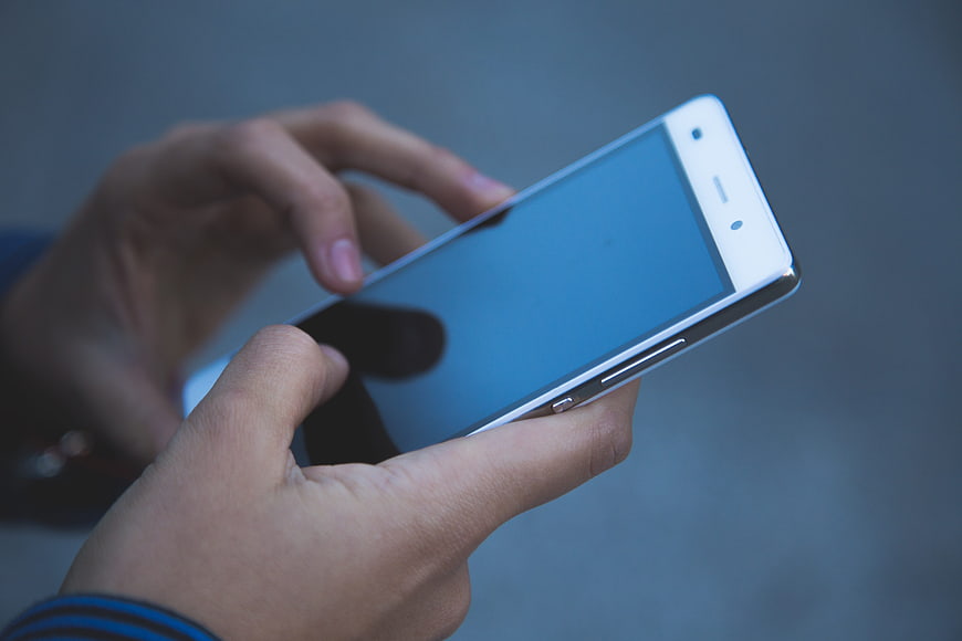 Close-up of hands holding white smartphone with blue screen