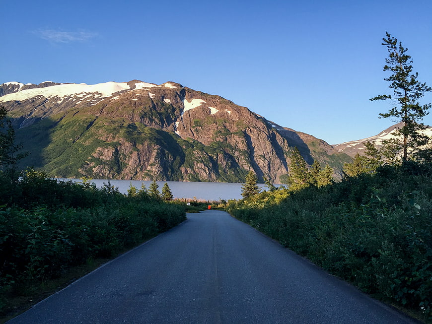 Scenic asphalt road leading to snow-capped mountains and lake