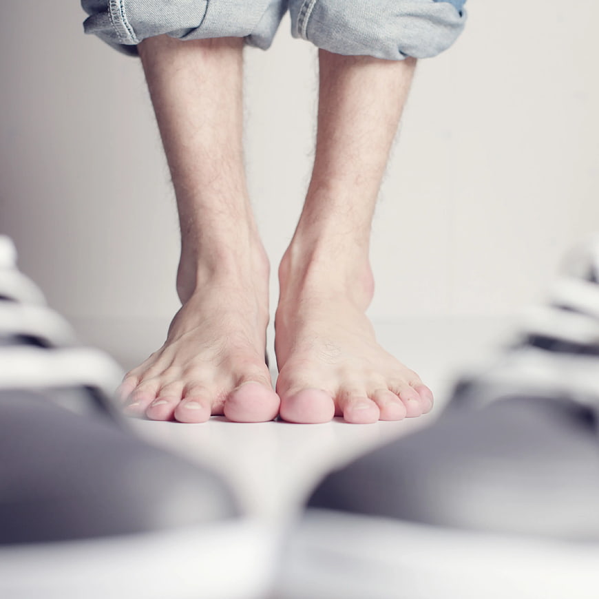Bare Feet Standing Between Sneakers