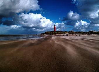 Red Lighthouse on Sandy Beach with Dramatic Clouds