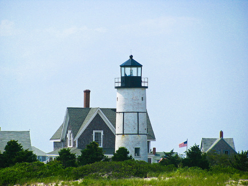 White Lighthouse with Coastal Houses and American Flag