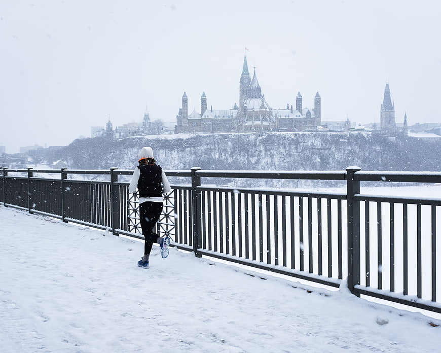 Woman Running on Snowy Path with Parliament Hill Background