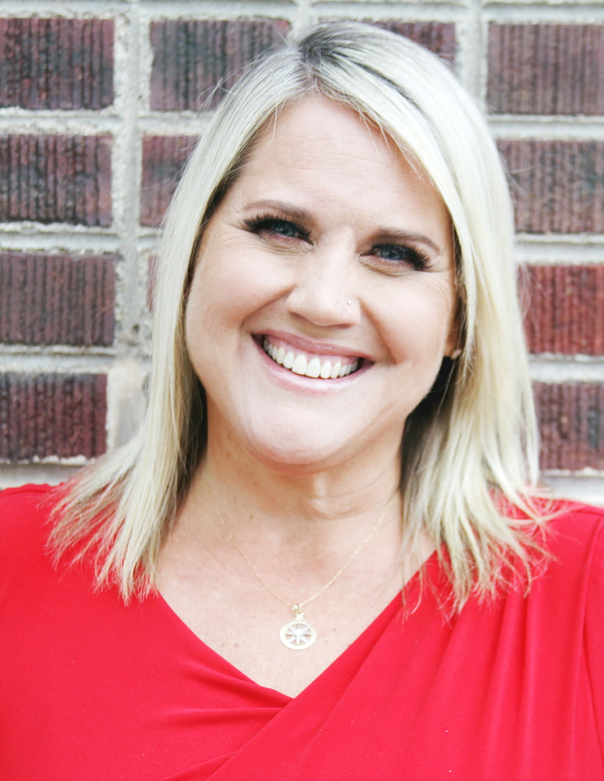 Smiling blonde woman in red top against brick wall