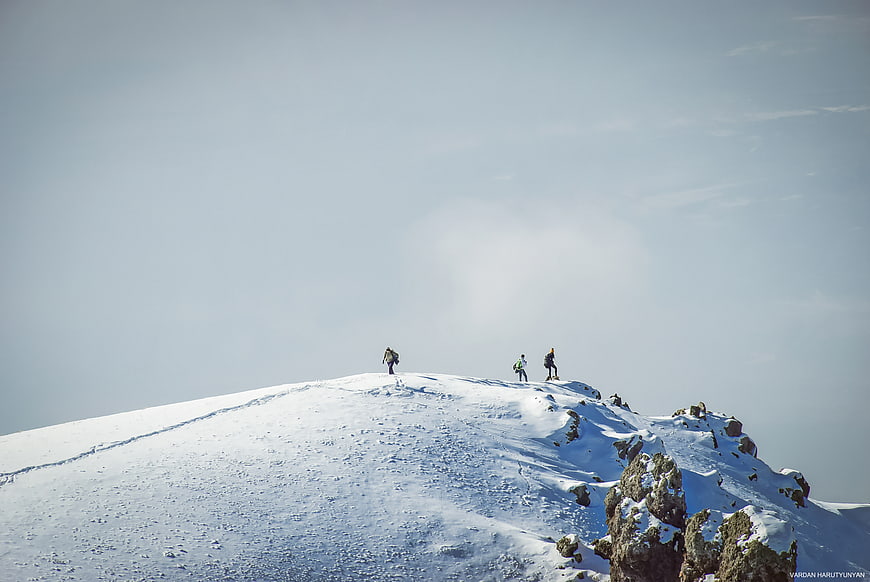 Hikers on Snowy Mountain Ridge Against Blue Sky
