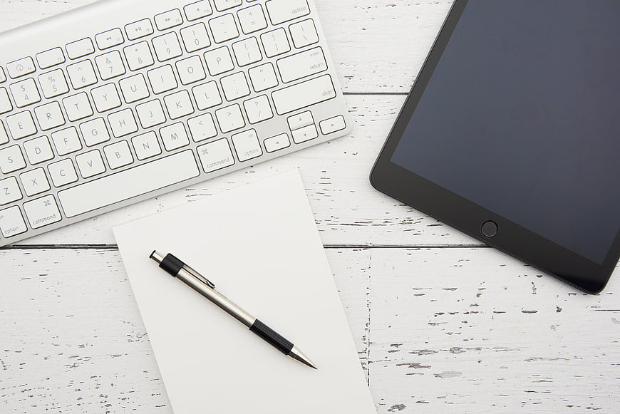 Top view of white workspace with keyboard, tablet, and pen
