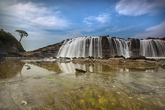Wide waterfall cascading over rocky cliffs into a clear stream
