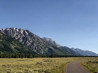 Paved path winding through grassy valley with mountains