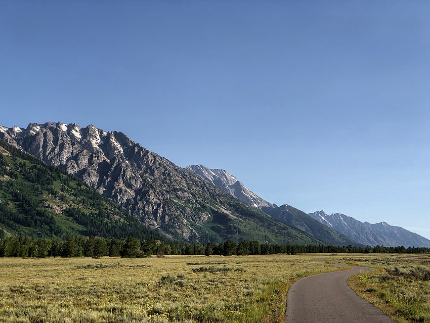 Paved path winding through grassy valley with mountains