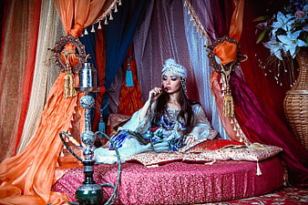 Woman in traditional dress smoking hookah in ornate harem setting