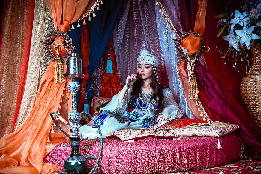Woman in traditional dress smoking hookah in ornate harem setting