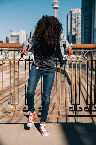 Man with dreadlocks leaning on rusty bridge railing in city