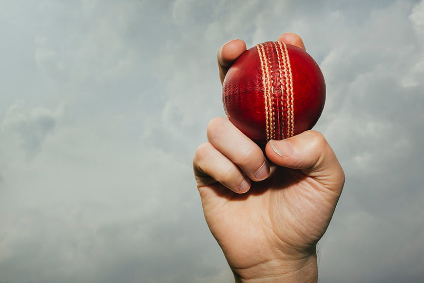Hand Holding Red Cricket Ball Against Cloudy Sky