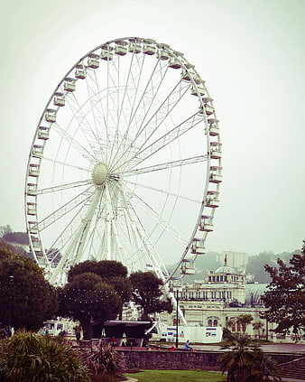 White Ferris Wheel in Overcast Sky with Park and Building
