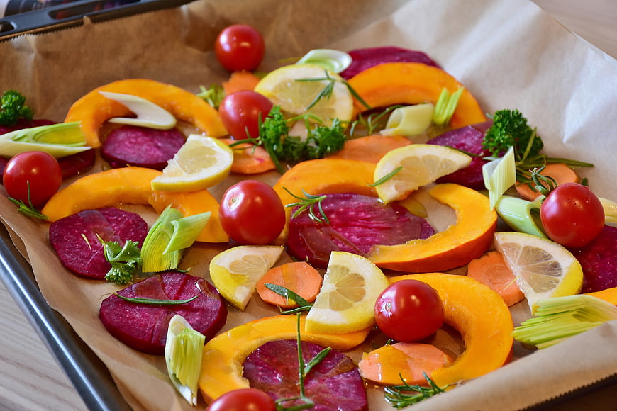 Raw autumn vegetables on baking sheet with lemon and herbs