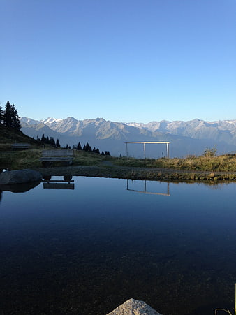 Serene mountain lake with bench and snow-capped peaks reflection