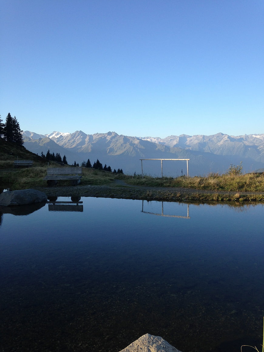 Serene mountain lake with bench and snow-capped peaks reflection