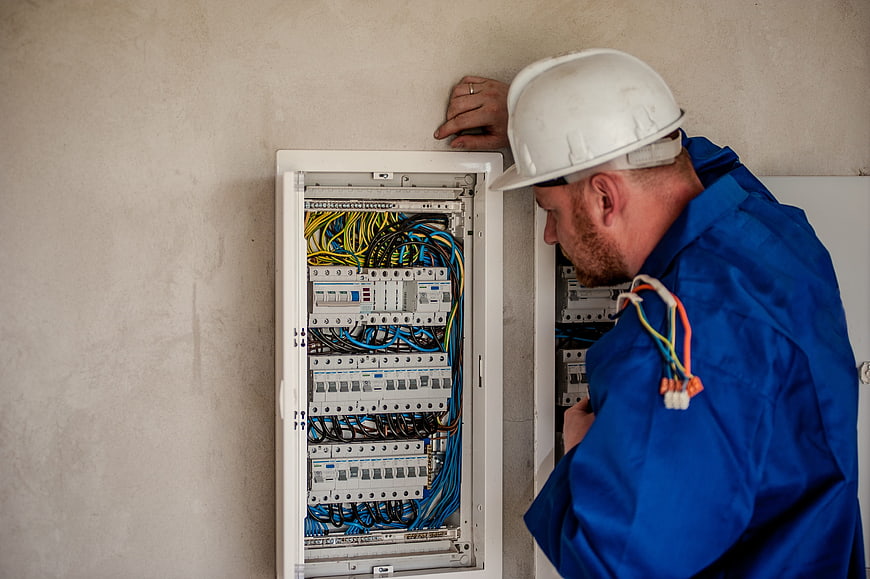 Electrician inspecting open electrical panel with wires