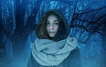 Mysterious woman in hooded cloak in snowy blue forest