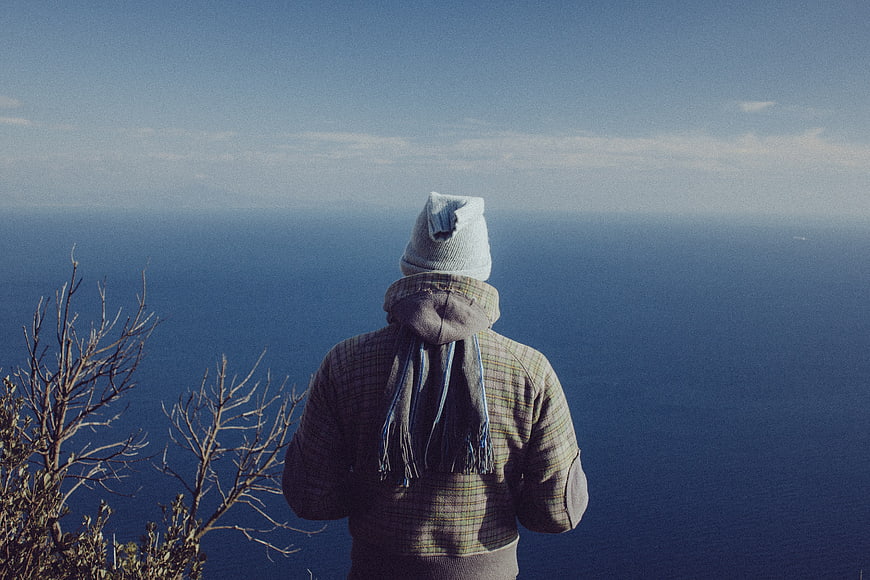 Man in Beanie Looking Out at Ocean from Cliff