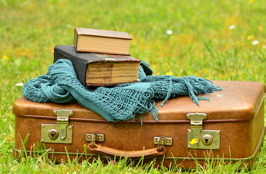 Vintage suitcase with old books and scarf on grass