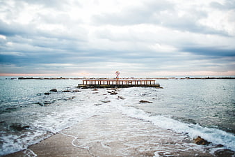 Serene coastal pier with gentle waves and overcast sky