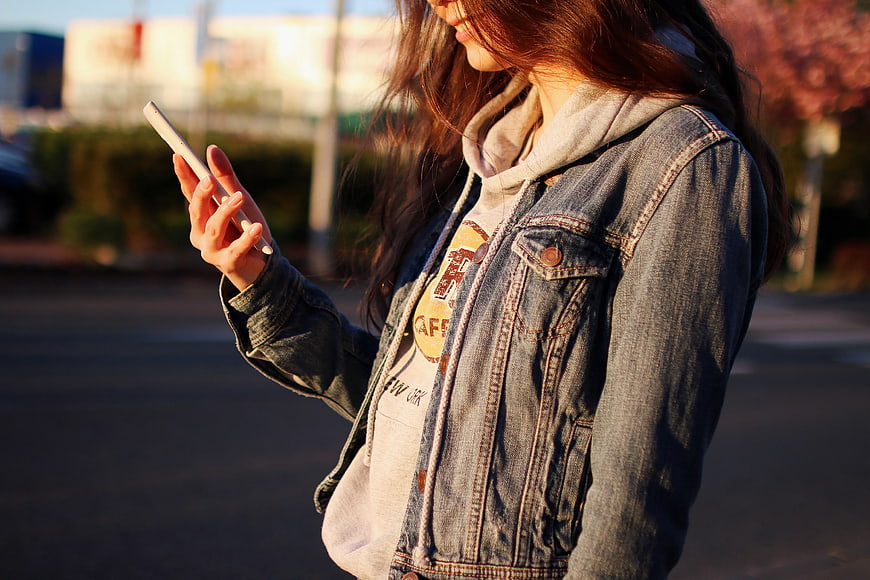 Young Woman Using Smartphone in Denim Jacket Outdoors
