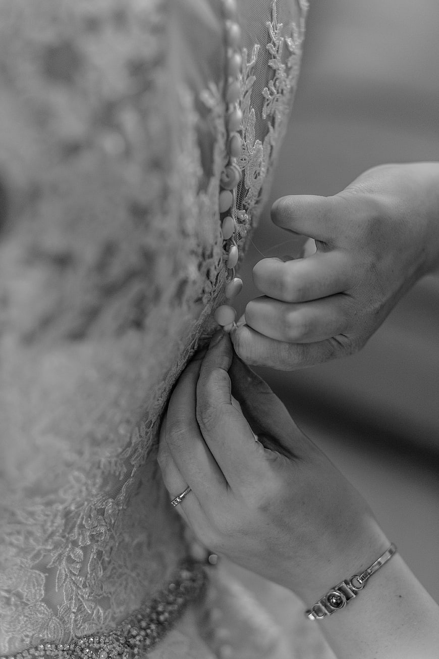 Close-up of hands buttoning a lace wedding dress