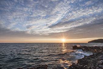 Sunset Over Rocky Coastline with Textured Clouds