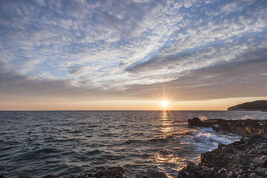 Sunset Over Rocky Coastline with Textured Clouds