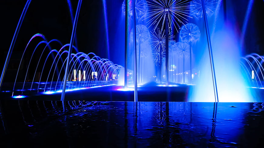 Blue illuminated fountain jets at night with water reflections